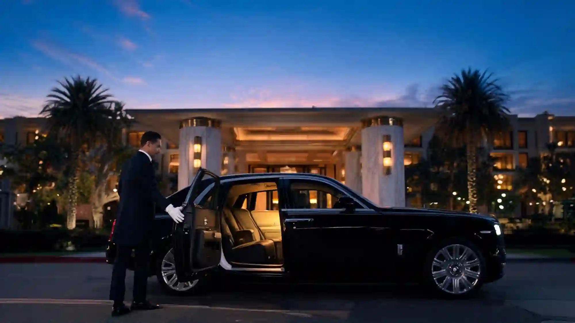 A chauffeur opening the door of a Rolls-Royce at a Los Angeles hotel at dusk